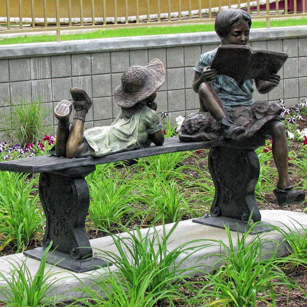 Boy reading history to cut girl on bench sculptures